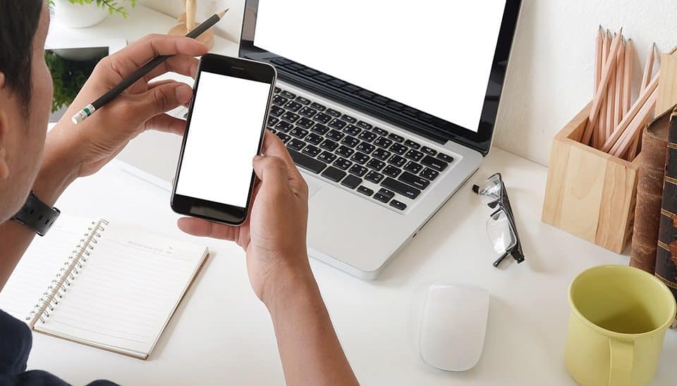 Man sitting at a desk doing research with a smartphone and laptop